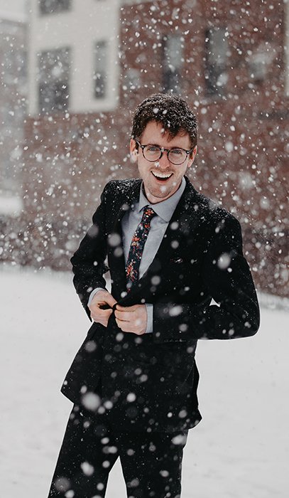Divertido retrato invernal de un modelo masculino posando casualmente bajo la nieve que cae