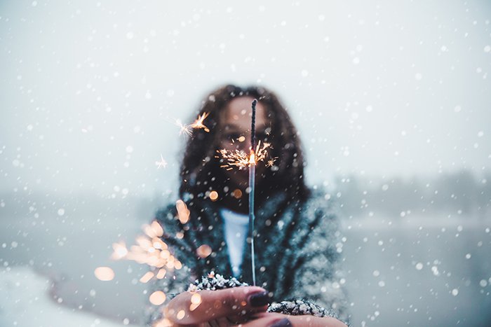 Atmósfera retrato invernal de una modelo femenina posando con bengalas bajo la nieve que cae por la noche