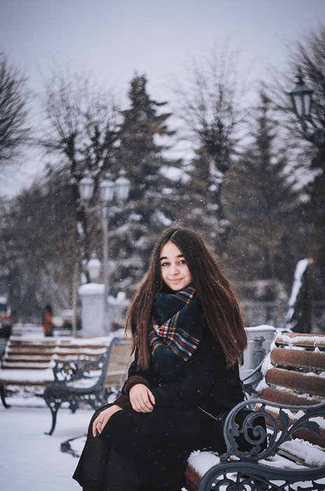Retrato de invierno atmosférico de una modelo femenina posando en un banco en la nieve que cae