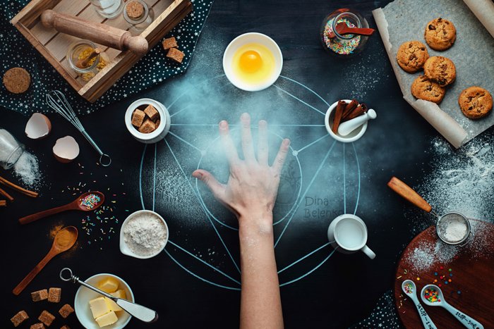 Fotografía cenital de una mano extendida en medio de un divertido arreglo fotográfico de comida sobre un fondo oscuro: ideas para la fotografía de bodegones.