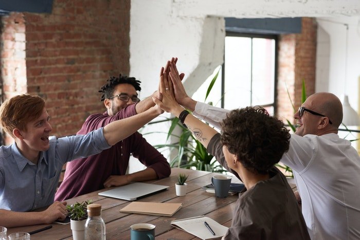 Cuatro compañeros de trabajo chocando los cinco en una mesa