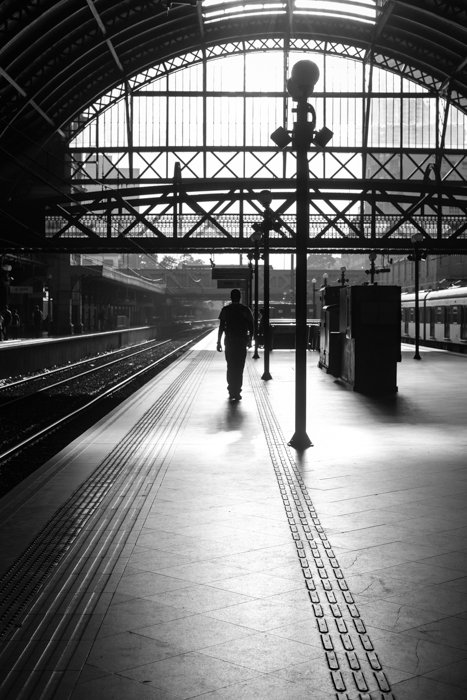 imagen en blanco y negro de un hombre caminando sobre un andén en una estación de tren