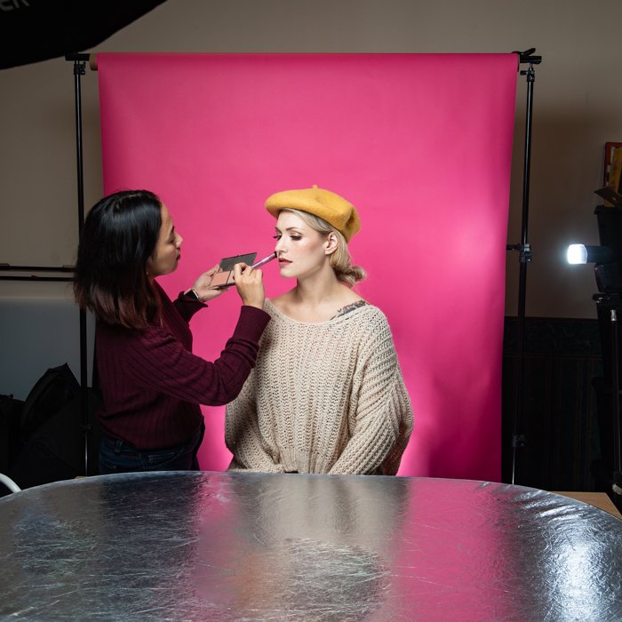 Una mujer maquillando a una modelo en un pequeño estudio.