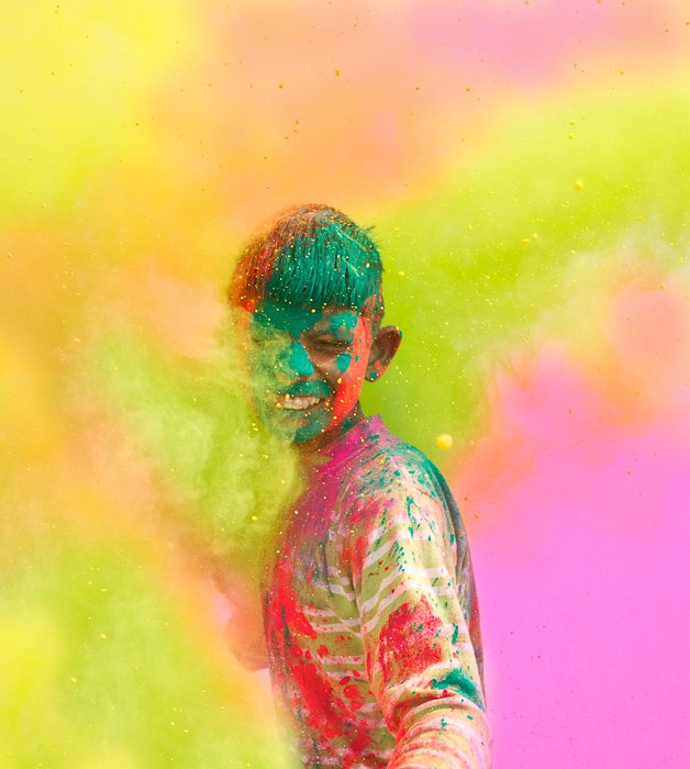 un niño cubierto de pintura de colores, parado en una nube de colores en un festival