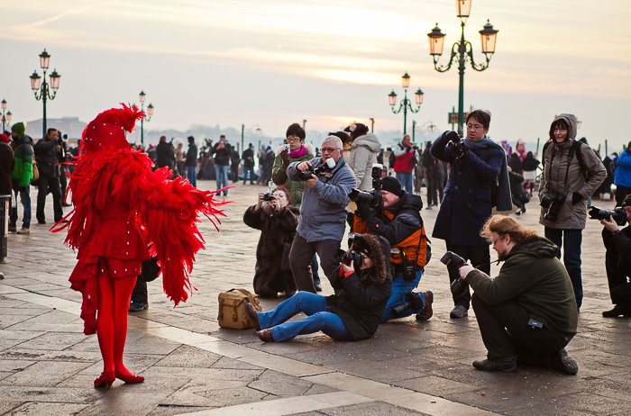 personas tomando fotos de un artista callejero con un traje rojo plumoso