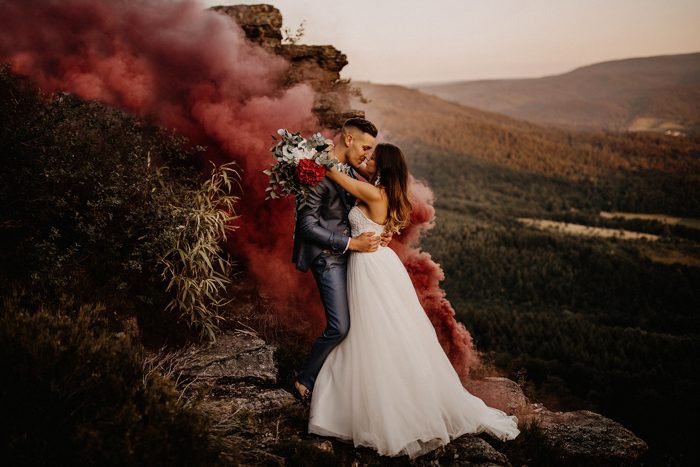 Una pareja de recién casados ​​abrazándose en un paisaje atmosférico con humo detrás de ellos del mejor blog de bodas, bodas de junio