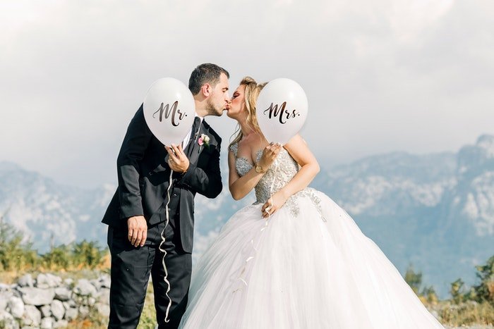Pareja de recién casados ​​besándose al aire libre y sosteniendo globos 'Mr & Mrs'