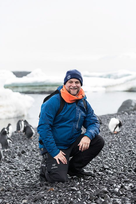 Un fotógrafo de vida silvestre sentado en una playa en medio de pingüinos - ropa de vida silvestre