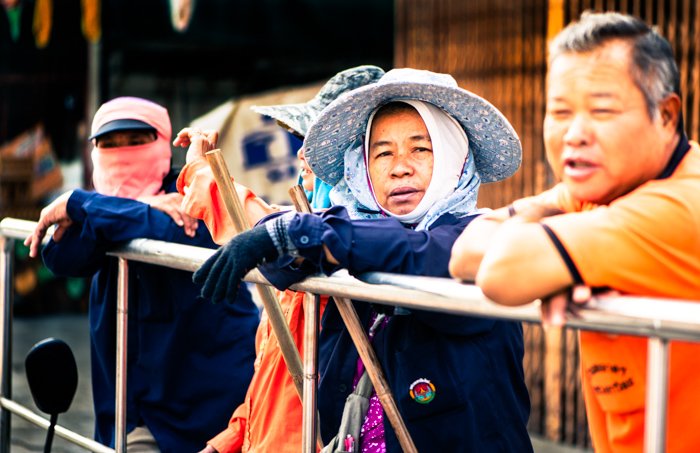 Un retrato callejero de algunos de los miembros del equipo de limpieza esperando detrás de las carrozas y los participantes durante el desfile anual de flores en Chiang Mai, Tailandia.  Consejos de fotografía narrativa