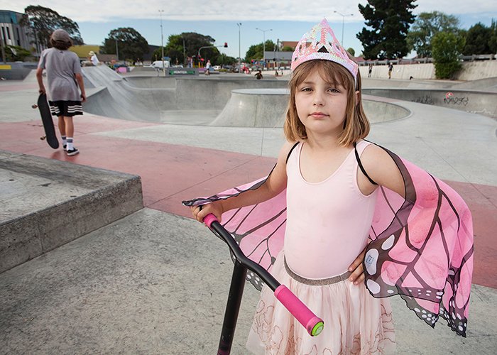 niñita con traje de mariposa princesa rosa con una moto, parque de patinaje en el fondo