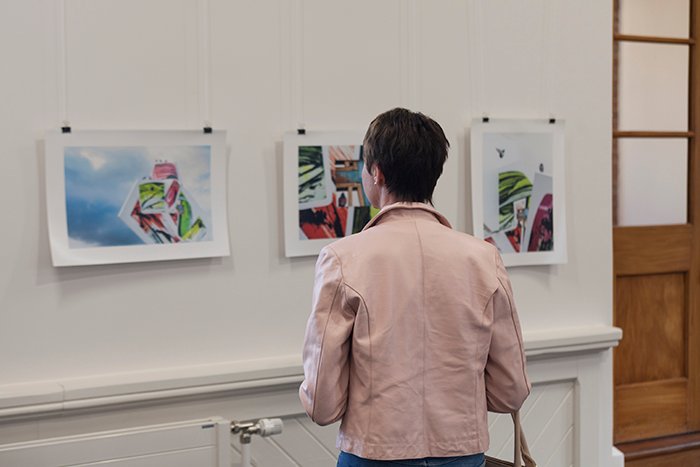 mujer con chaqueta rosa mirando pinturas en una exposición de arte