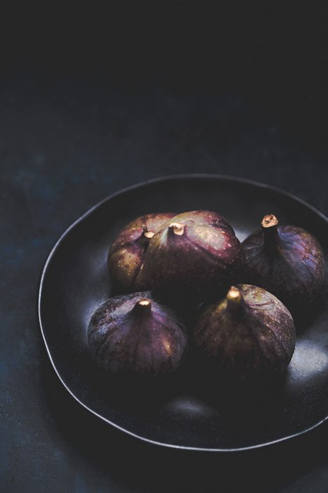 Fotografía de alimentos de un plato de higos frescos contra un fondo oscuro.