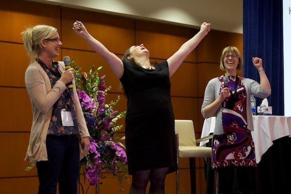 Una mujer mostrando alegría entre dos mujeres en el escenario - Fotografía de eventos corporativos