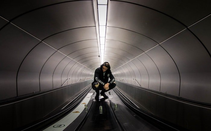 El hombre se pone en cuclillas en un túnel subterráneo con cintas transportadoras como idea para poses masculinas