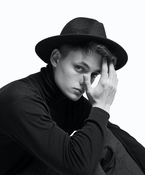 Foto de estudio en blanco y negro de una modelo con sombrero y tocándose la cara como idea para poses masculinas