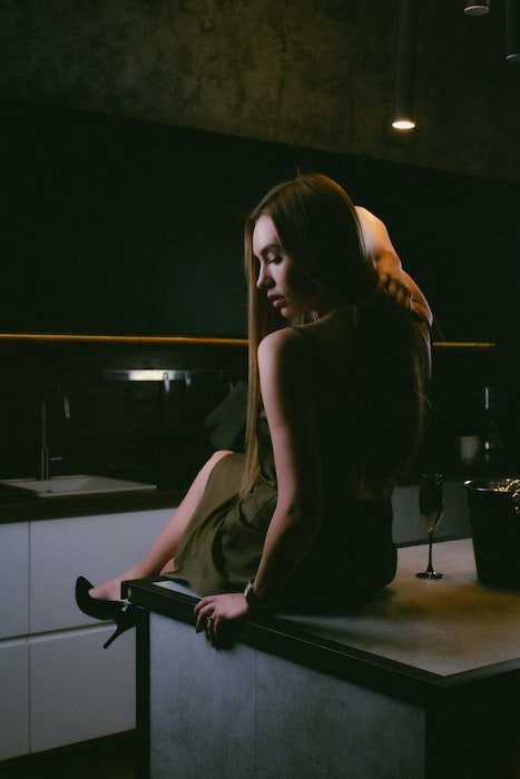 Idea de pose de modelo con una mujer sentada en una cocina mirando hacia abajo y sobre su hombro