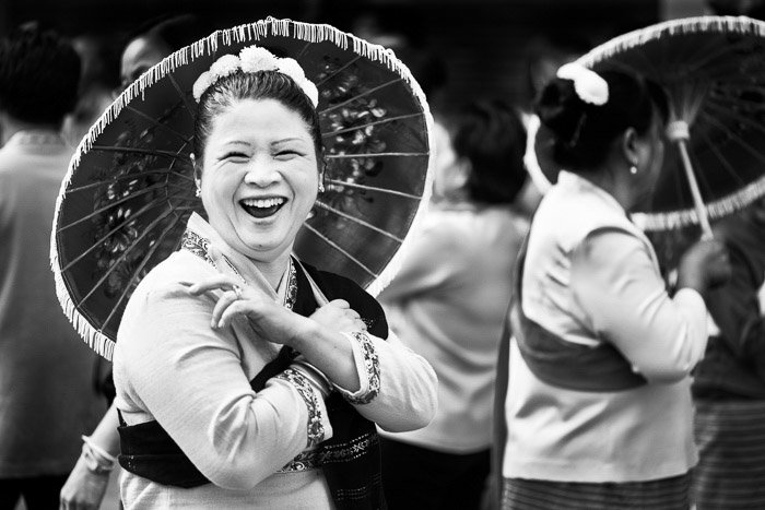 Un retrato callejero en blanco y negro de una mujer con un paraguas riendo con amigos antes del comienzo del desfile anual de flores.  Consejos de fotografía narrativa
