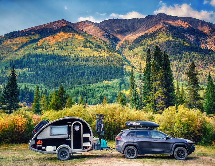 Un coche tirando de una caravana en forma de lágrima frente a un hermoso paisaje