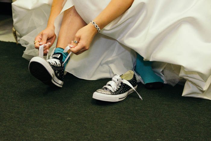 foto de detalles de una novia atando los cordones de sus zapatos converse debajo de su vestido de novia