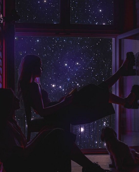 Dos personas y un gato sentados frente a una ventana estrellada.