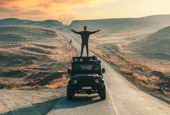 fotografía de aventura de un hombre parado encima de un camión mientras conduce por el desierto