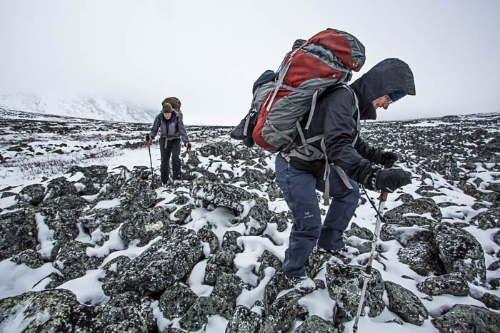 una imagen de dos personas con mochilas caminando en montañas cubiertas de nieve