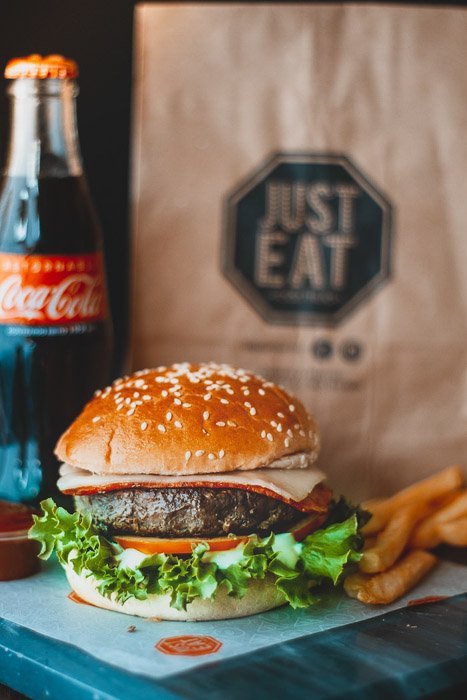 Una deliciosa hamburguesa junto a un refresco y una bolsa de papel para alimentos