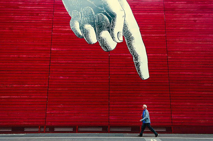 Una fotografía conceptual de un hombre caminando bajo una imagen enorme de un dedo señalador