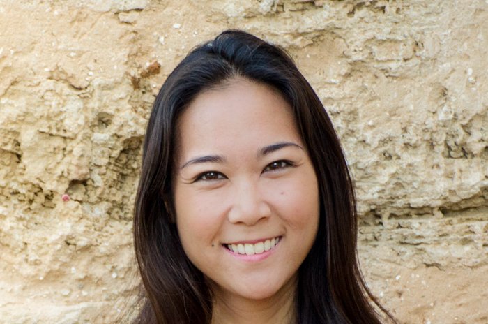 Una foto de una mujer asiática sonriente frente a una pared de piedra arenosa