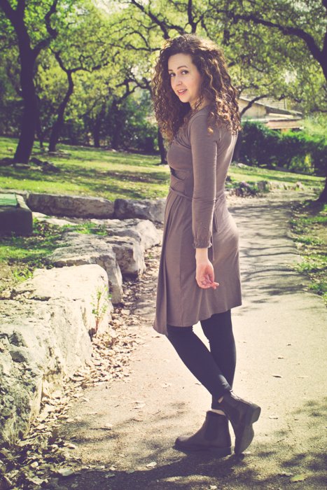 morena de cabello rizado con un vestido marrón y botas mirando hacia atrás mientras camina por un camino de tierra en un parque - recortando fotos