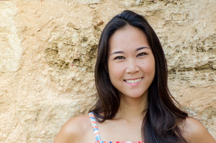 foto recortada debajo de los hombros de una mujer asiática sonriente frente a una pared de piedra arenosa
