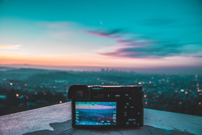 una imagen de una cámara sin espejo colocada en una repisa con vista al horizonte de la ciudad al atardecer