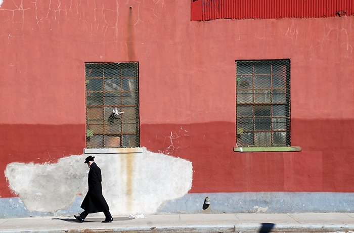 Una fotografía de bellas artes de un hombre caminando por la calle pasando una pared roja