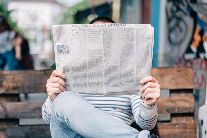 Un plano directo de un hombre sentado en un banco leyendo un periódico