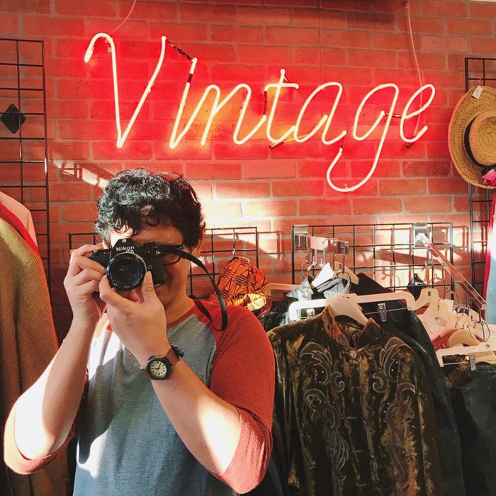Fotografía de retrato de un hombre en una tienda de ropa vintage sosteniendo una cámara.  Consejos de Instagram para fotografía de redes sociales.