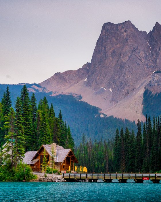 Foto de una casa de madera junto a un puente sobre aguas azules con un fondo montañoso.  Composición de fotografía de paisaje