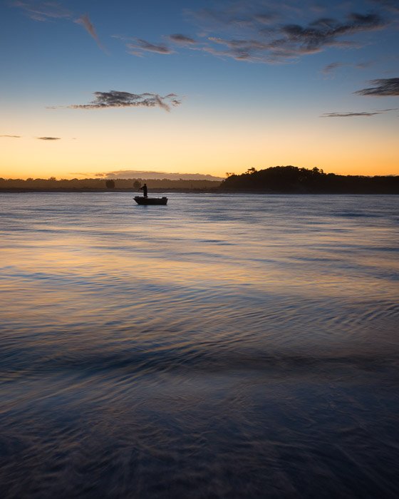 Una figura en un pequeño bote sobre el agua al atardecer.  Composición de fotografía de paisaje