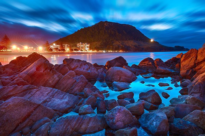 Una fotografía asombrosamente coloreada de un primer plano rocoso con una montaña y un cielo nocturno dramáticamente iluminado en el fondo.  Uso del primer plano para la composición de fotografías de paisajes