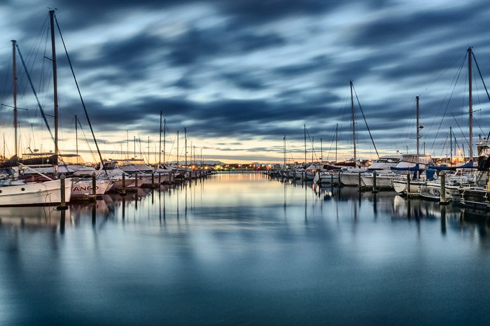 Una foto de barcos alineados en el puerto bajo un espectacular cielo nublado.  Simetría en la composición de la fotografía de paisaje