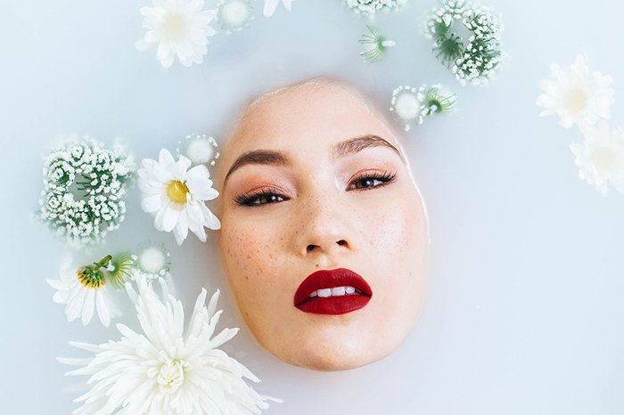 Hermosa fotografía de baño de leche de una modelo femenina rodeada de flores blancas