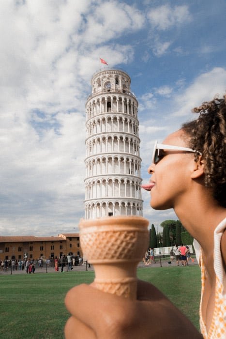 Divertida fotografía en perspectiva forzada de una niña posada para que parezca que está lamiendo la torre inclinada de Pisa en un cono de helado