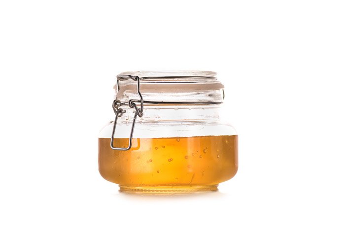 Una fotografía de producto de un tarro de miel sobre fondo blanco.