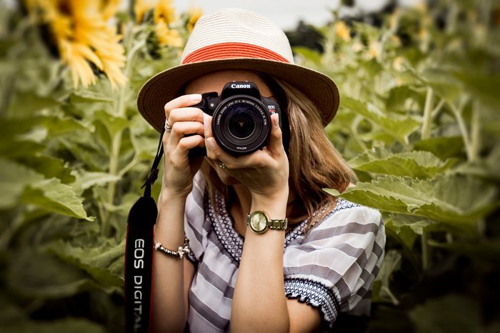 Una niña en un campo de girasoles tomando una foto con una cámara DSLR