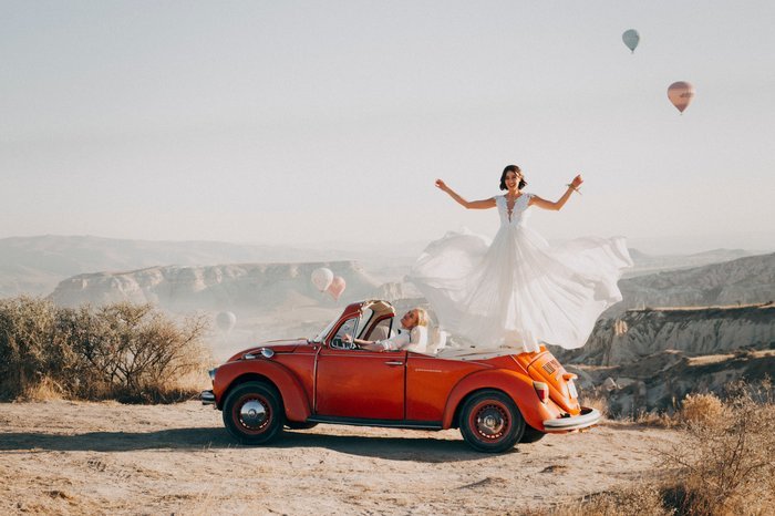 Divertido retrato de boda de la novia parada en la parte trasera de un auto en el desierto
