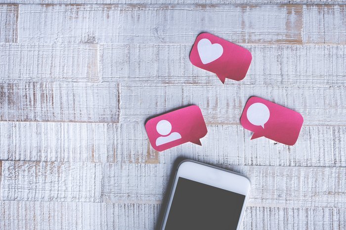 Un teléfono inteligente con globos de diálogo recortados encima con íconos de redes sociales en ellos