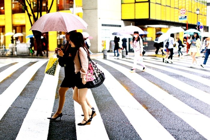 Fotografía de viaje de dos mujeres con sombrillas cruzando la calle, concurrida escena callejera de fondo.