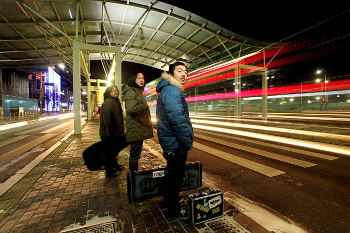 Retrato urbano de tres personas esperando el transporte público por la noche