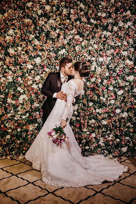 Una novia y un novio besándose frente a una pared floral