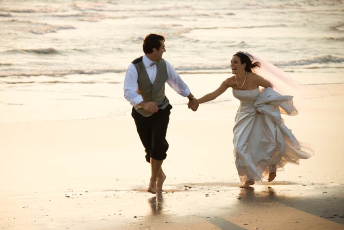 Una imagen del novio y la novia corriendo en la playa