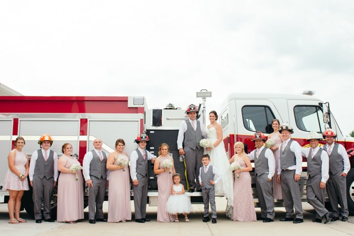 Una foto de grupo de bodas posada en cascos de bombero por un camión de bomberos